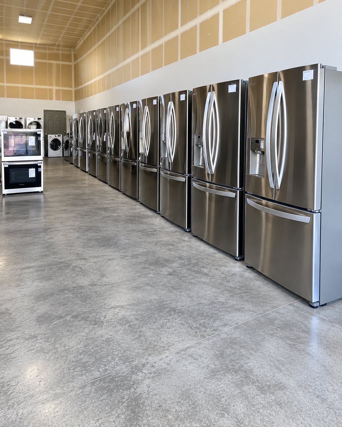 Showroom display of stainless steel refrigerators lined up against wall with appliances on left side