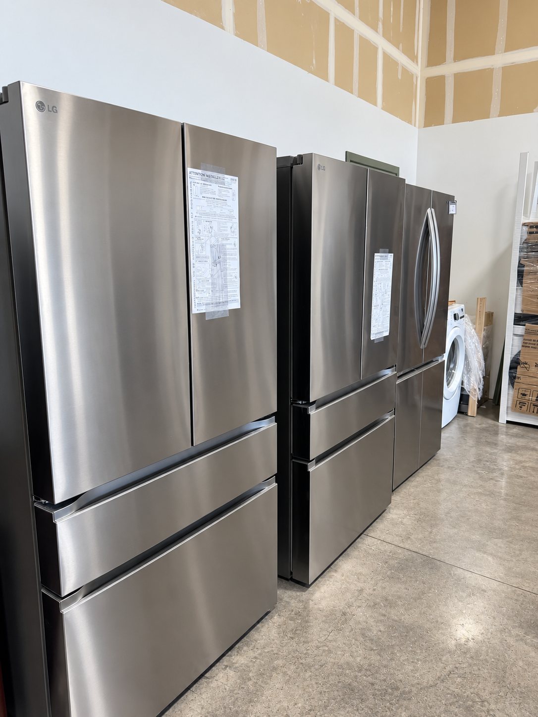 Multiple stainless steel refrigerators displayed in a showroom with specification tags attached