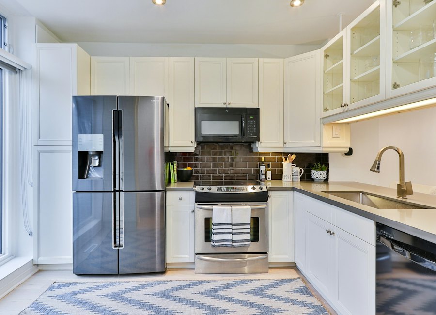 Modern kitchen with white cabinets, stainless steel appliances, dark subway tile backsplash, and blue geometric floor rug